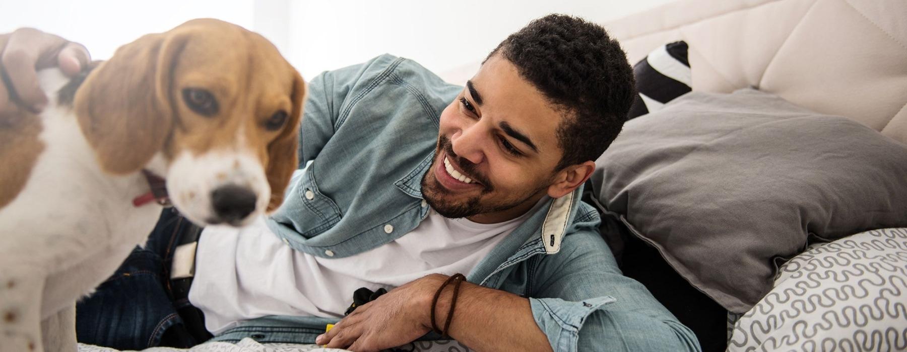 man smiles and pets his dog on a bed