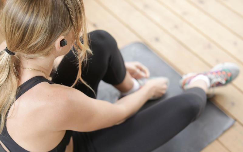 woman in workout gear, sits on a yoga mat and ties her shoe